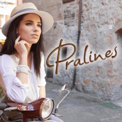 Longhaired woman in a hat sits on the scooter and looks ahead, on the front of the photo is the logotype: Pralines