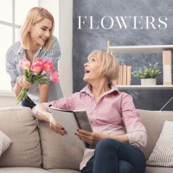 Two blond woman talks with each other, one of them has flowers in hand, second one sits on the couch, on the front of the photo is the text: Flowers