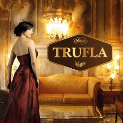 Woman in a long red dress looks somewhere, standing in a fancy room, on the front of the photo is the logotype: Trufla