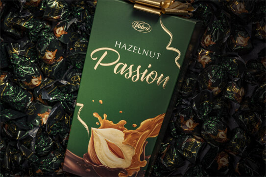 Opakowanie Hazelnut Passion od Vobro na tle pralin w zielonych zawijkach