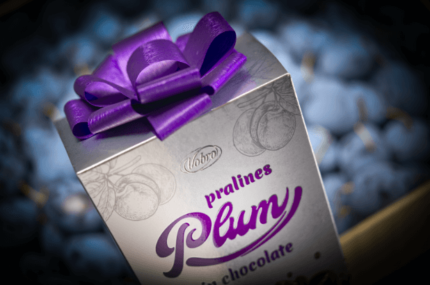 Pralines Plum in Chocolate gift 192 g package in front of the plums